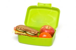 A picture of a container with a sandwich on whole grain bread with meat and vegetables, along with a peach and an apple.